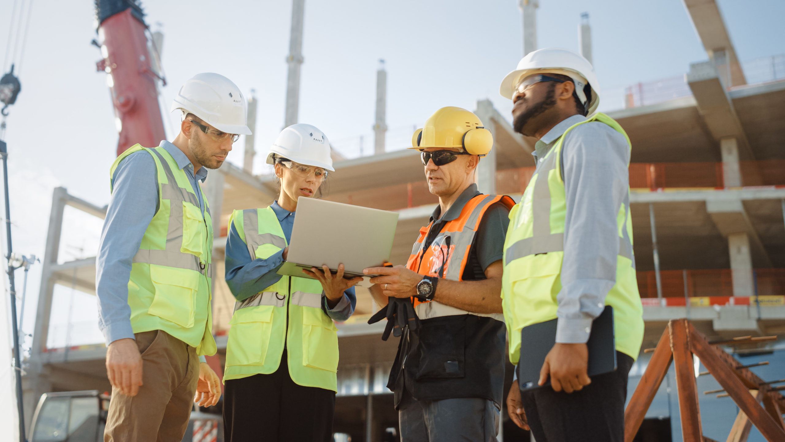 Diverse Team of Specialists Use Laptop Computer on Construction Site. Real Estate Building Project with Machinery: Civil Engineer, Investor, Businesswoman and Builder Discussing Blueprint Plan