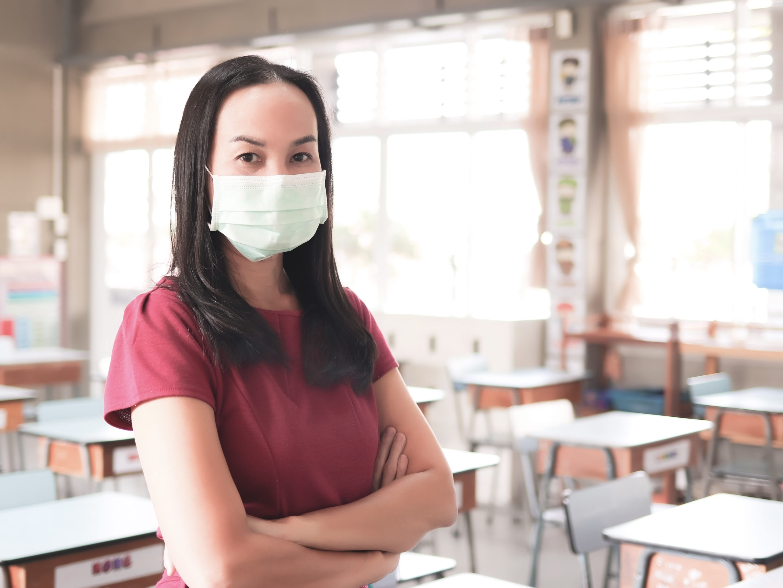 Asian female teacher wearing protective face mask, standing in e